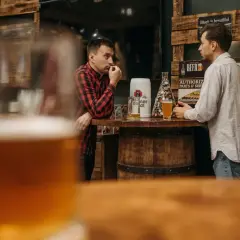 Dwóch mężczyzn rozmawia przy barze. Na blacie stoi kufel i szklanka piwa. Ciekawe, ile schodzi jedno piwo w takim miejscu.