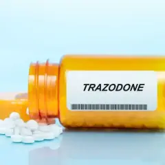 Pomarańczowa butelka z tabletkami trazodone, kilka białych tabletek rozsypanych obok.