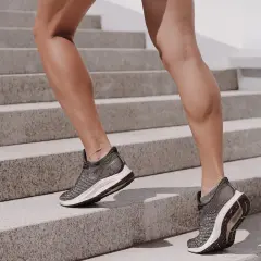Nogi w butach sportowych wspinają się po schodach. Widać napięcie mięśni, lekkie drżenie mięśni świadczące o wysiłku.