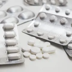 Opakowania tabletek, w tym blister z lekami, być może seronil, i luźno rozsypane białe tabletki na białym tle.