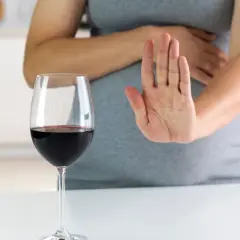 Kobieta w ciąży odrzuca kieliszek czerwonego wina, mówiąc "nie" alkoholowi.