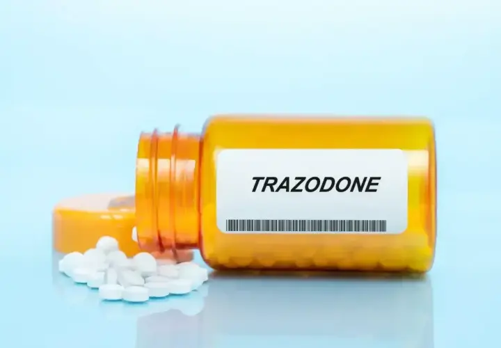 Pomarańczowa butelka z tabletkami trazodone, kilka białych tabletek rozsypanych obok.