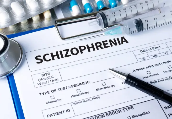 Lekarz wypełnia dokumentację medyczną dotyczącą schizofrenii, obok leków, w tym risperidon, strzykawek i stetoskopu.