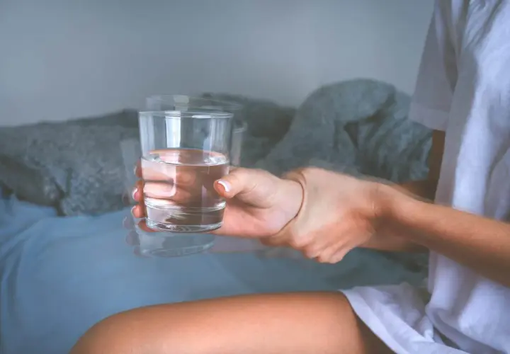 Drżąca ręka trzymająca szklankę wody, symbolizująca objawy padaczki alkoholowej.