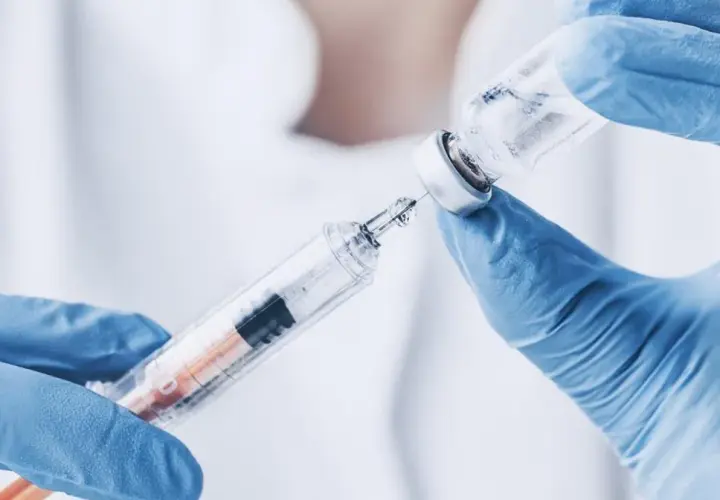 Ręce w niebieskich rękawiczkach pobierają płyn z fiolki do strzykawki. To może być propofol, środek znieczulający.
