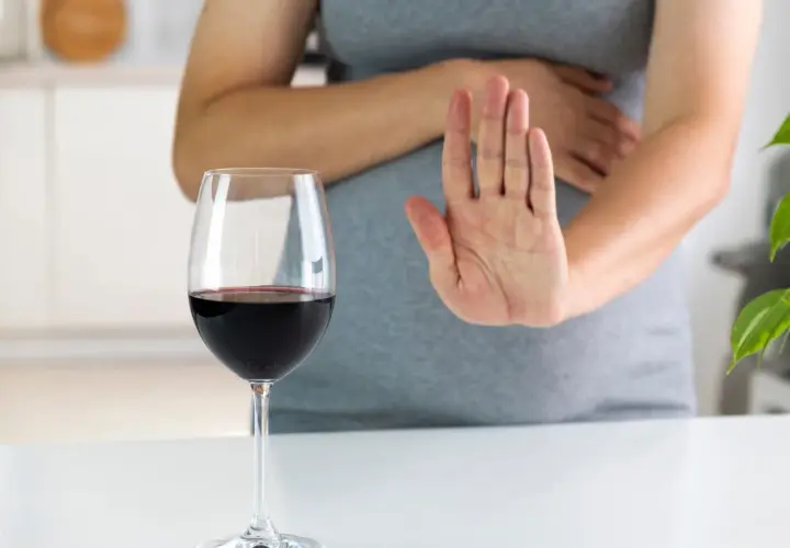 Kobieta w ciąży odrzuca kieliszek czerwonego wina, mówiąc "nie" alkoholowi.