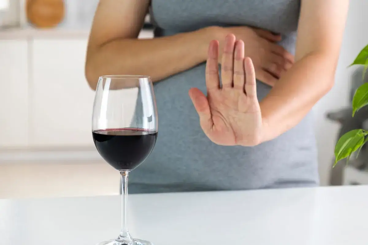 Kobieta w ciąży odrzuca kieliszek czerwonego wina, mówiąc